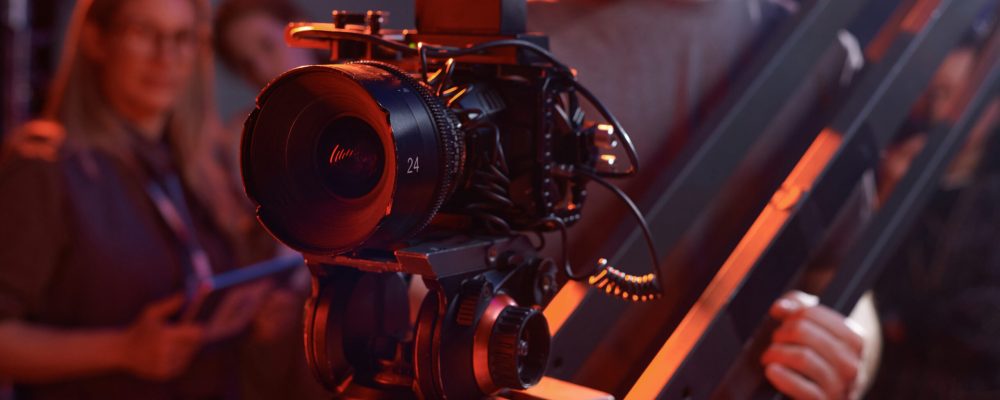 Closeup of cameraman operating video camera on rig in studio with red neon lights copy space